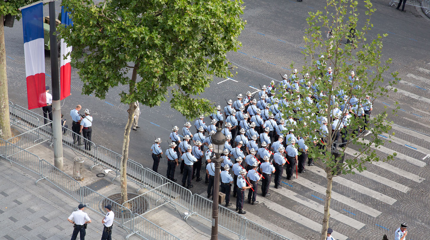 Veduta ampia dell'Avenue des Champs-Élysées preparata per la parata, con transenne metalliche e bandiere francesi tricolori lungo il percorso