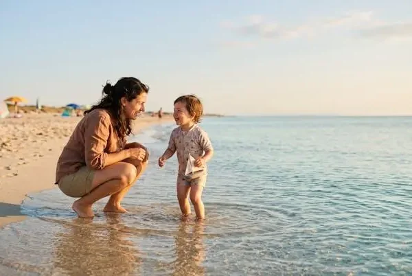 Genitore e bambino che giocano insieme in acqua bassa e trasparente su una spiaggia sabbiosa al tramonto