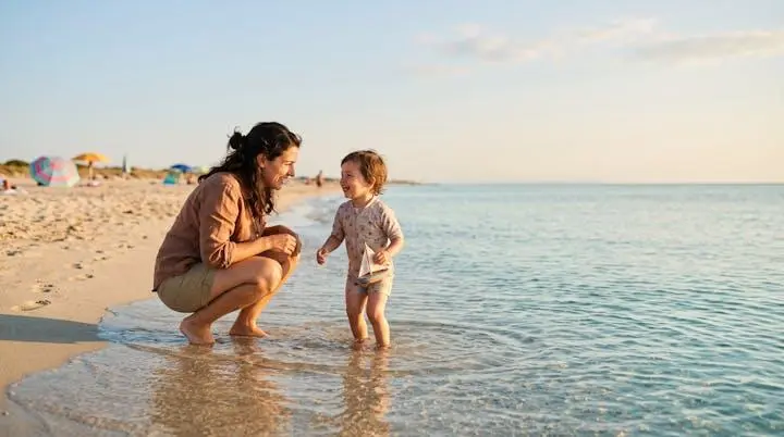 Genitore e bambino che giocano insieme in acqua bassa e trasparente su una spiaggia sabbiosa al tramonto