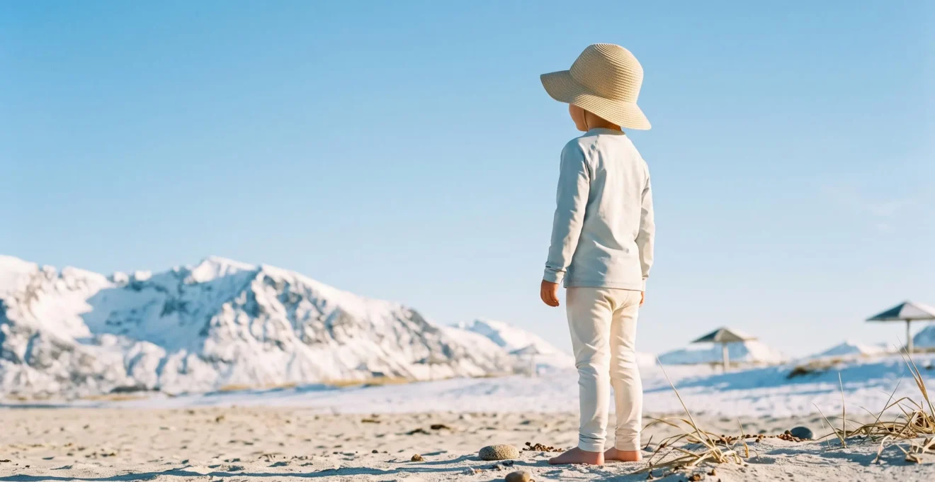 Bambino con cappellino e crema solare che gioca in un paesaggio che unisce simbolicamente montagna innevata e mare, protetto dal sole
