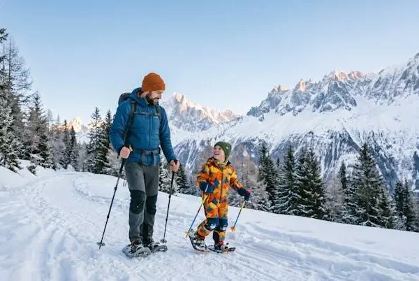 Famiglia con bambino piccolo che cammina con le ciaspole su un sentiero di montagna innevato al mattino