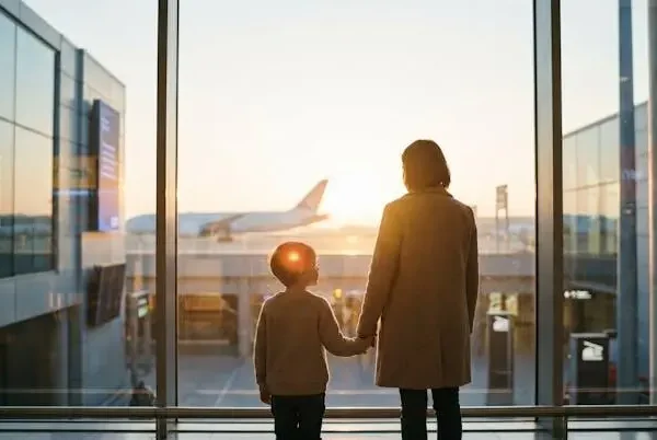 Famiglia con bambino piccolo che osserva un aereo attraverso la vetrata di un aeroporto al tramonto