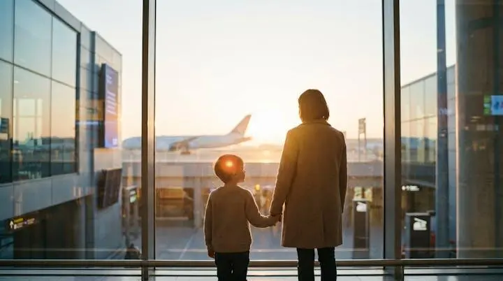 Famiglia con bambino piccolo che osserva un aereo attraverso la vetrata di un aeroporto al tramonto