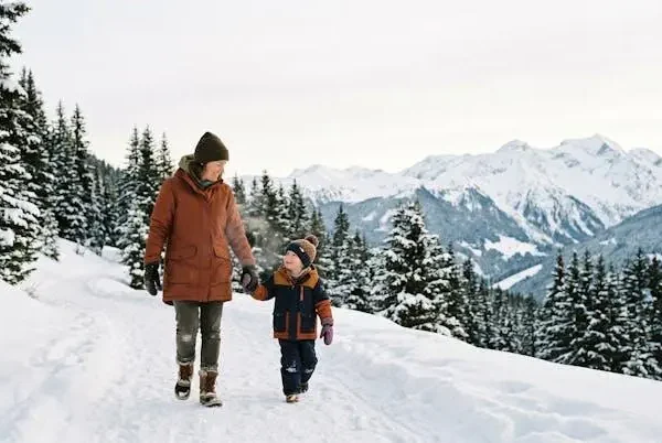 Genitore e bambino con ciaspole camminano felici su un sentiero di montagna innevato circondato da abeti