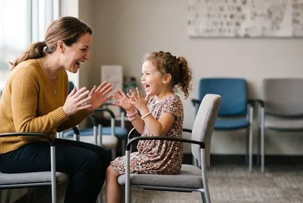 Genitore e bambino sorridenti che giocano insieme con la sola fantasia in una sala d'attesa, senza oggetti né schermi